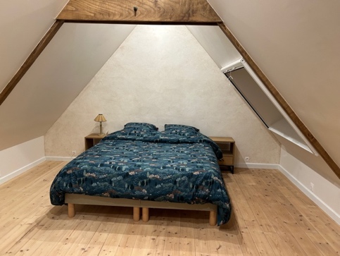 Le lit double sous les poutres à l’étage, sur un plancher en bois